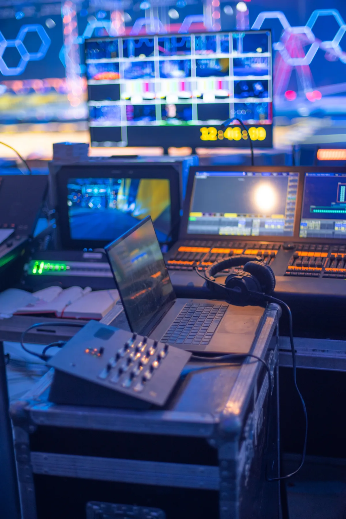 Front-of-house production desk at a live event: lighting console, monitors, laptop and headset on a road case.